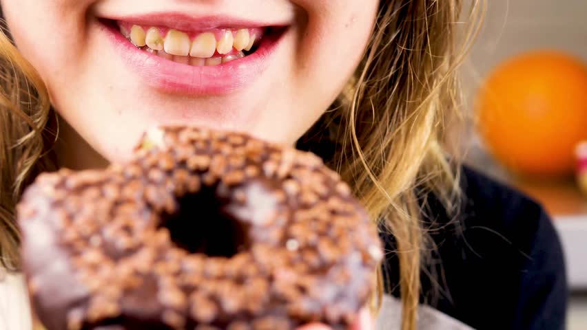 Close up of Woman biting into chocolate donut covered in sprinkles, holding treat in hands. Bright colorful snack, sweet tooth, dessert craving. food backgrounds
