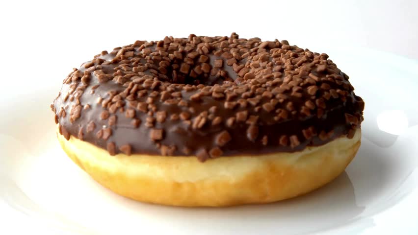Chocolate donut with smooth frosting and crunchy chocolate sprinkles sits on a white plate, perfect for dessert lovers craving a delicious treat.