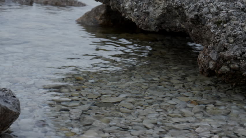 A beautiful, static time-lapse video clip showing a close-up perspective of clear water ripples and small, smooth round rocks glistening under the surface along the shore of Lake Michigan.