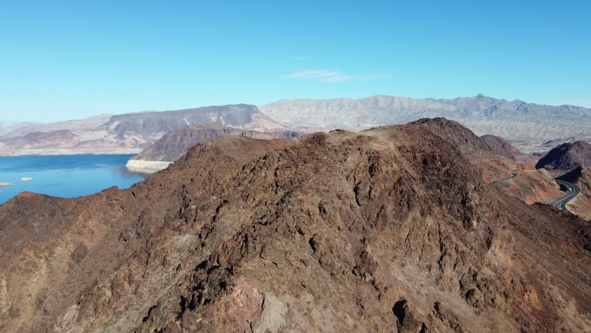 Lake Mead and rugged desert mountains near Hoover Dam in Nevada, Aerial travel video follows winding roads above blue water and volcanic ridges
