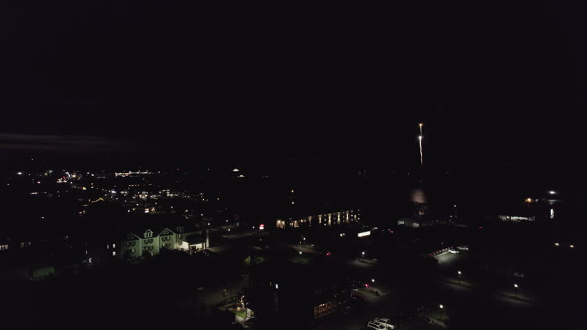 A spectacular aerial drone video clip hovering over the water at night, capturing patriotic red, white, and blue fireworks launching from a barge in Mackinaw City, Michigan for America