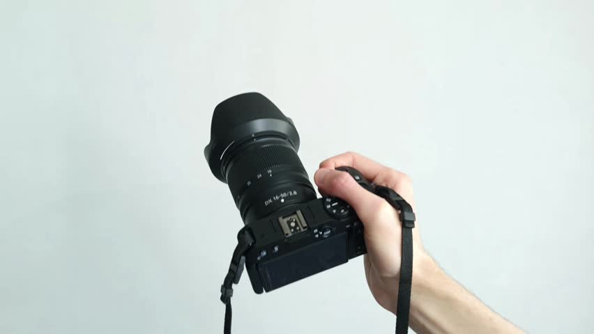 Human hand firmly holds professional camera with lens hood pointing forward on white background