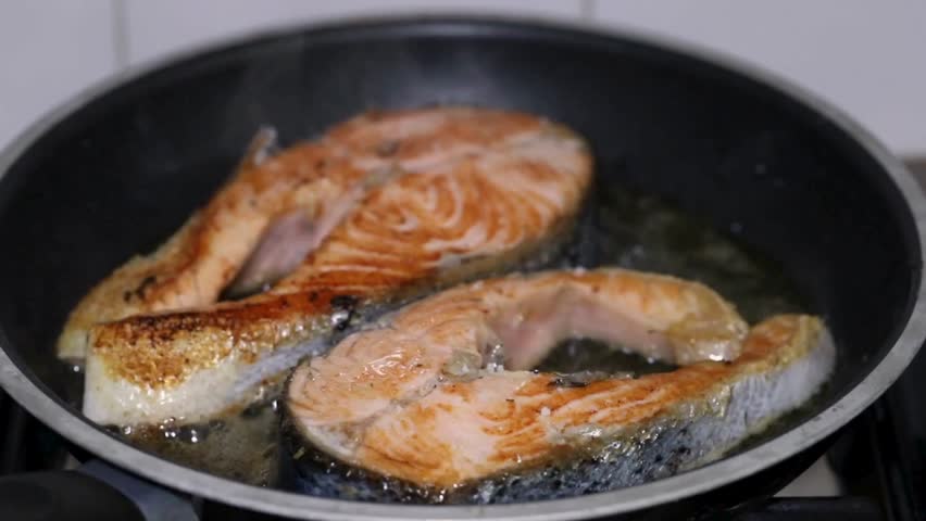 Salmon fillets sizzling in hot oil in a frying pan, showcasing mouthwatering colors and cooking process in a bright kitchen atmosphere.