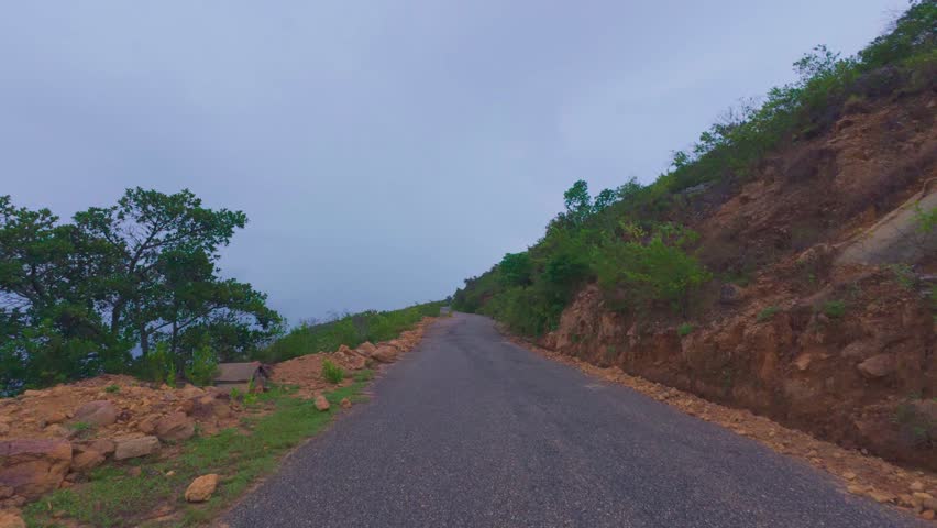 Narrow empty paved mountain road winding through a picturesque landscape under a cloudy sky