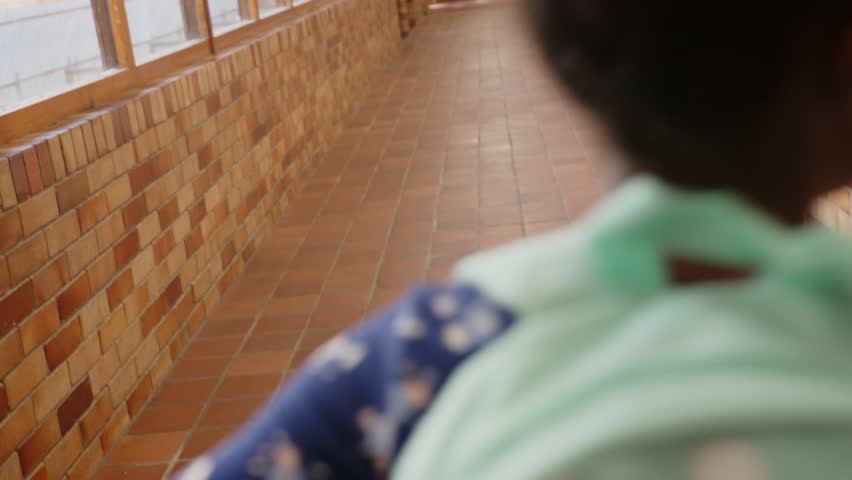 Camera pulling back two girls hand-in-hand going down school hall to exit, packs, pencils drifting. Friendship, students, duo, animated, vibrant, daylight, corridor