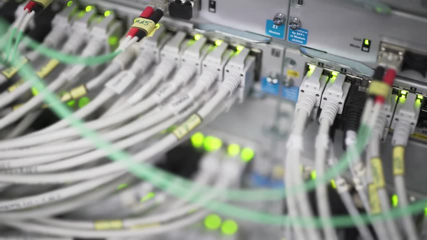 Zoomed view of network cables plugged into servers in a data center. Bright LED lights blink to show active connections and data flow within the server infrastructure.