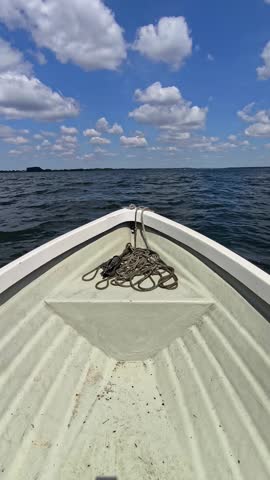 View from the bow of a moving boat cruising on a wide lake under a blue cloudy sky
