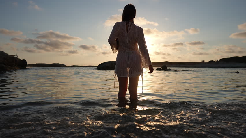 Attractive young woman with long hair dancing in slow motion in the sea during sunset. Beautiful silhouette of a girl on the beach