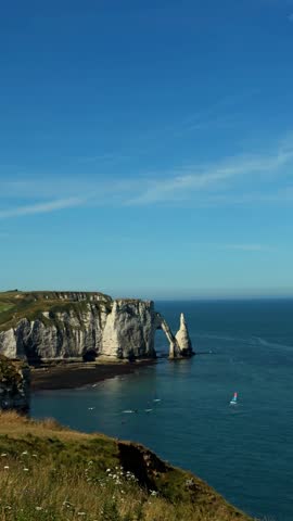 Beautiful scenic overlook of famous chalk arch cliffs in Etretat Normandy France on sunny day with people windsurfing on turquoise sea water.