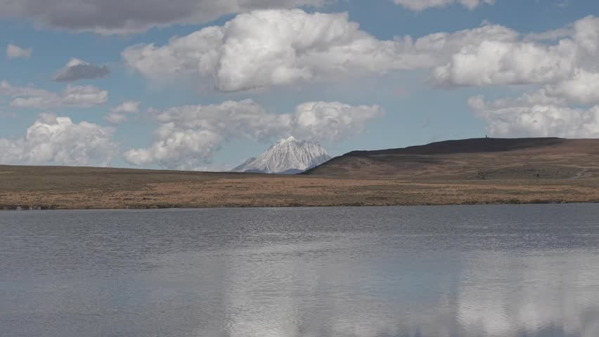 Calm lake with distant snow capped mountain beyond open moorland beneath dramatic clouds. Peaceful natural scenery in Scotland United Kingdom during daytime