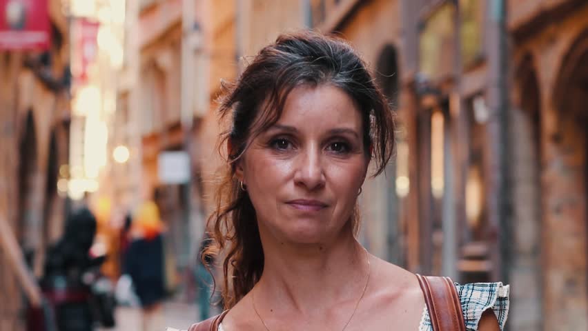 Portrait of a happy middle aged brunette woman with a backpack looking at the camera and smiling while visiting a historic old town