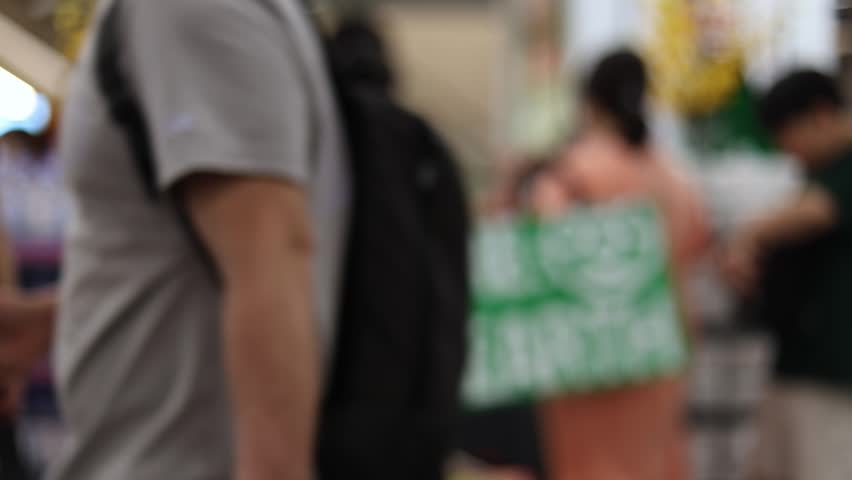 Blurred background of crowd of shoppers with carts choosing food products inside supermarket. Out of focus abstract bokeh of people in grocery store. Retail and consumerism concept.