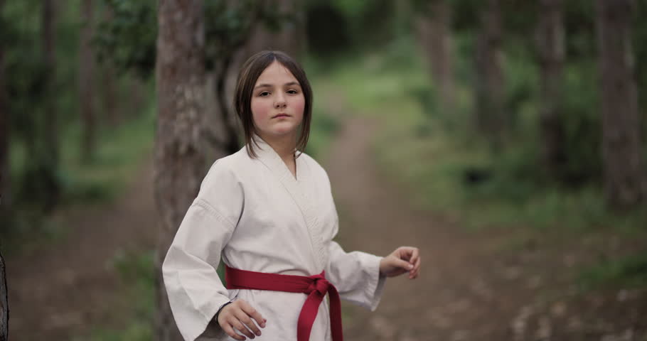 A determined young girl practices karate in nature, showing strength and precision in her martial arts training.
