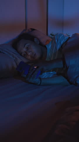 Man browsing social media on a smartphone in bed at night with the lights off, representing excessive screen time, bedtime routine, insomnia, and mobile phone addiction.