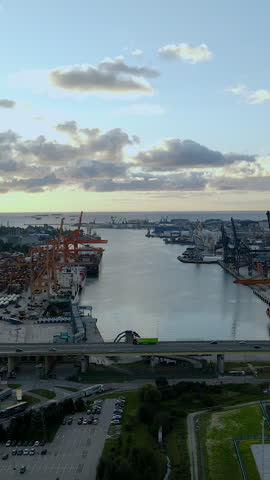 Cinematic aerial shot of the industrial port in Gdynia, Poland, featuring cargo ships, cranes, and the Estakada Kwiatkowskiego bridge during golden hour.