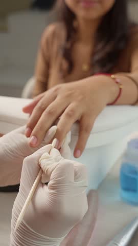 Professional manicurist in gloves using a wooden stick to push back the cuticles on a client