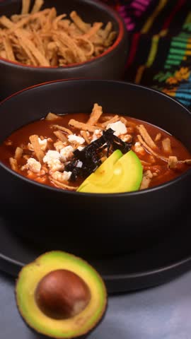 Mexican food, hand adding sour cream over a black bowl of authentic Mexican tortilla soup