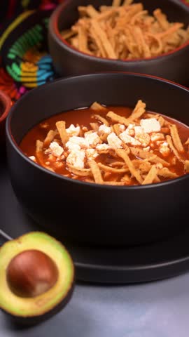 Mexican food, hand preparing an authentic Mexican tortilla soup with avocado slices
