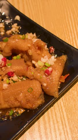 Close-up shot of chopsticks picking up braised chicken feet garnished with garlic and chili.