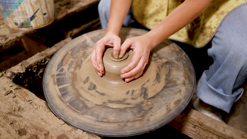 Artisan hands mold wet clay on a spinning pottery wheel in a traditional workshop setting.