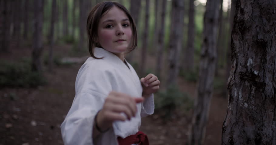 A determined young girl hones her martial arts skills, practicing karate punches in a peaceful forest setting.
