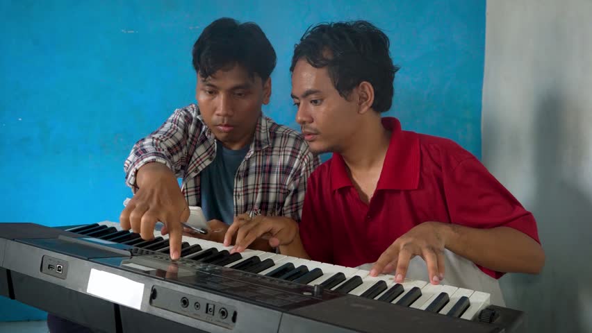 Two Men Learning Piano Together With A Digital Tablet In A Room With Blue Walls