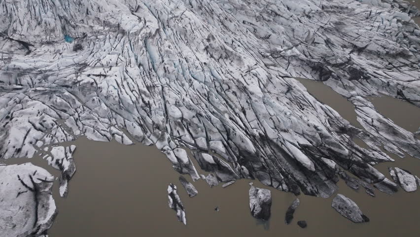 Aerial view of glacier meeting muddy meltwater lake, dramatic ice patterns visible