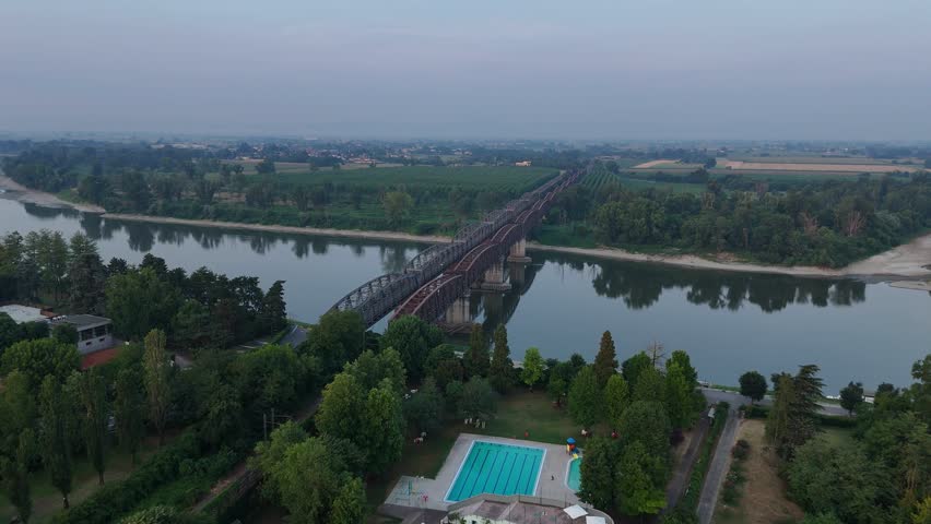 Ponte di Ferro crossing the Po River between Cremona, Lombardy, and Castelvetro Piacentino, Emilia-Romagna, Italy, with Canottieri Leonida Bissolati outdoor swimming pool in the foreground, aerial