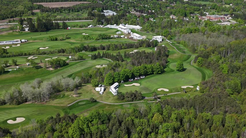 Dynamic aerial footage captures sprawling golf course with manicured greens, fairways, sand traps, and surrounding dense forest, offering a serene landscape.