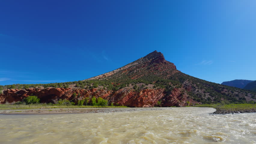 Isolated desert butte rises above the Yampa River under clear blue skies, backcountry pack rafting experience through the river rapids