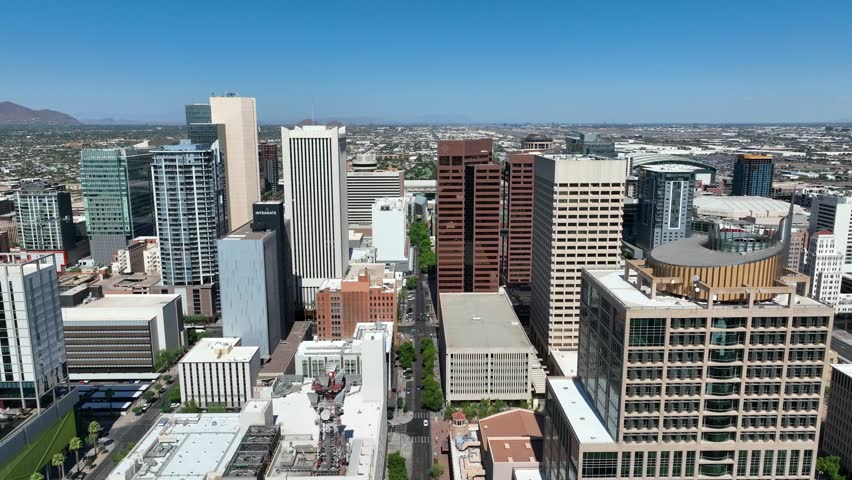 Dynamic aerial drone footage captures bustling downtown Phoenix city skyline featuring high rise office buildings urban infrastructure city streets and bright sunny weather for professional projects.