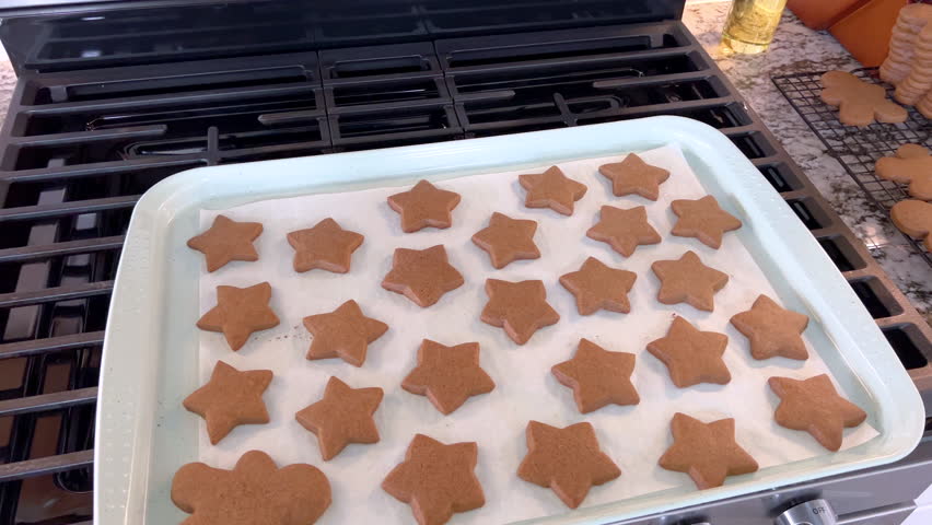 Wide shot of a baking tray on a stovetop lined with parchment and covered in star shaped cookies. The cookies appear evenly baked with a light brown surface under bright kitchen lighting. The frame