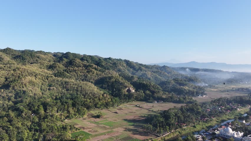 Wide aerial footage of rolling hills and trees under blue sky