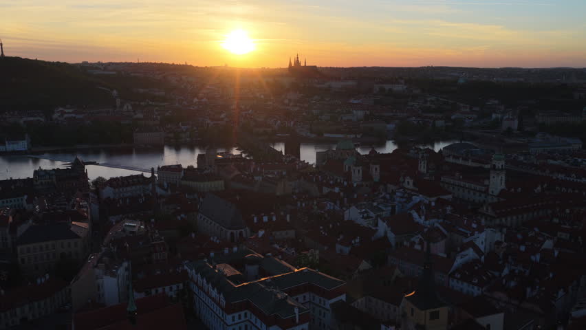 Aerial drone view of the Vltava river and Charles Bridge with Prague Castle and St. Vitus Cathedral silhouetted at sunset, Prague, Czech Republic.
