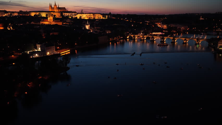 High-altitude aerial view of Prague Castle, Charles Bridge, and the Vltava river at dusk with a glowing pink and orange sunset sky, Prague, Czech Republic.