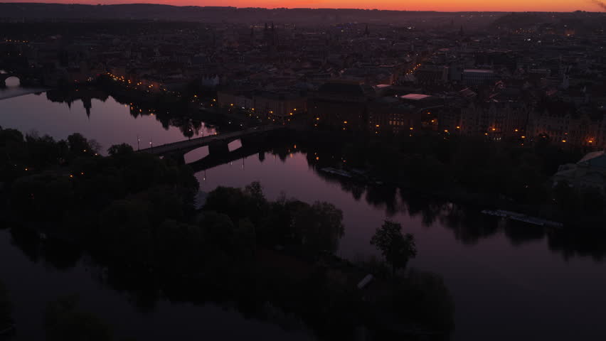 Aerial drone view of Prague at vivid orange sunset with the Vltava river and a bridge in the foreground, historic old town silhouetted on the far bank, Prague, Czech Republic.