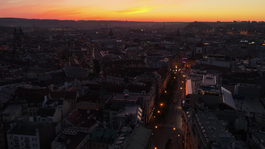Aerial drone view of the old town at deep orange-red sunset, dense historic rooftops and church spires silhouetted across a wide panorama.