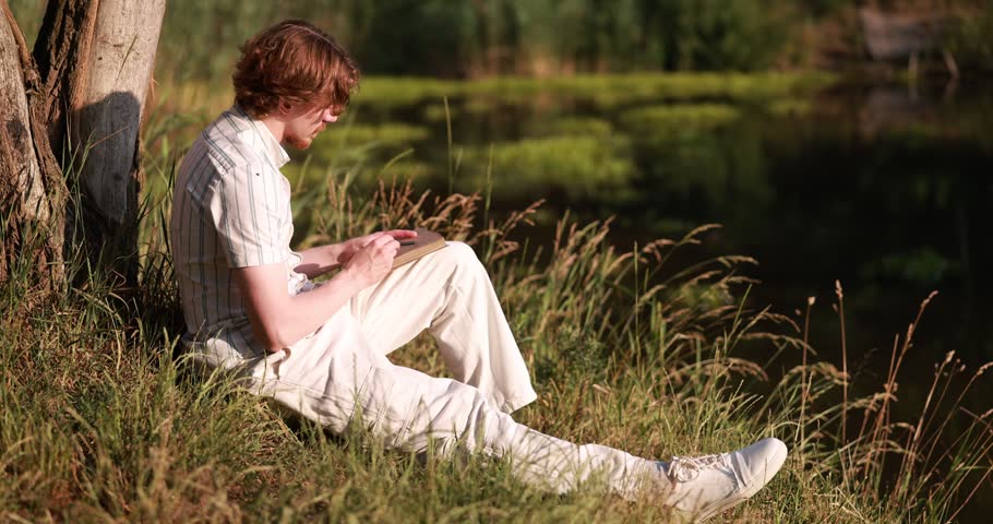 Man drawing sketch for future painting in meadow. Artist working outdoors