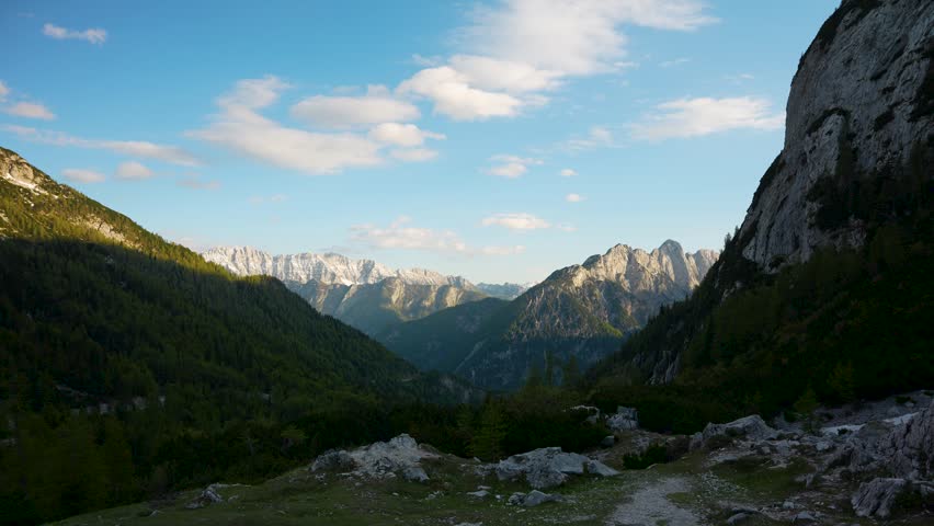 Clouds moving above the Julian Alps near Vršič Pass, Slovenia, with rugged mountain peaks and forested valleys during golden hour, timelapse