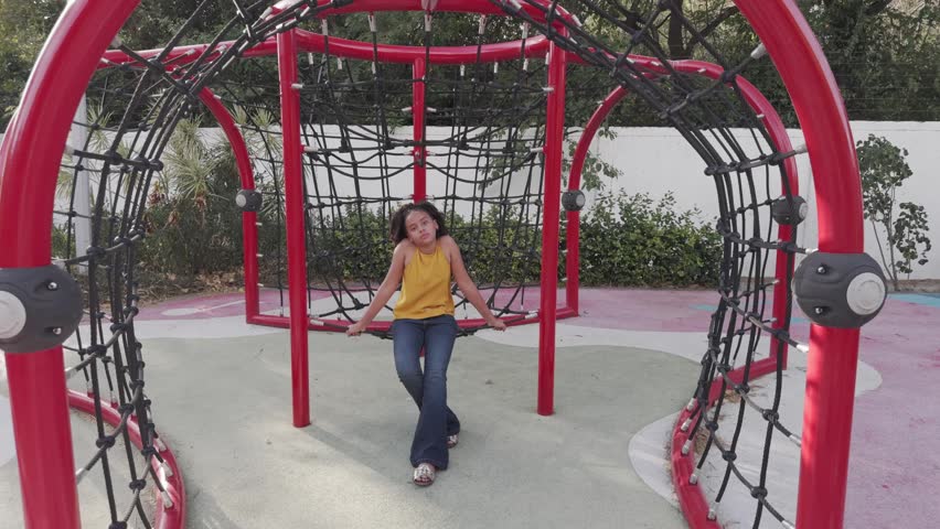Charming teenage girl with curly hair walking towards the camera and smiling in an urban playground