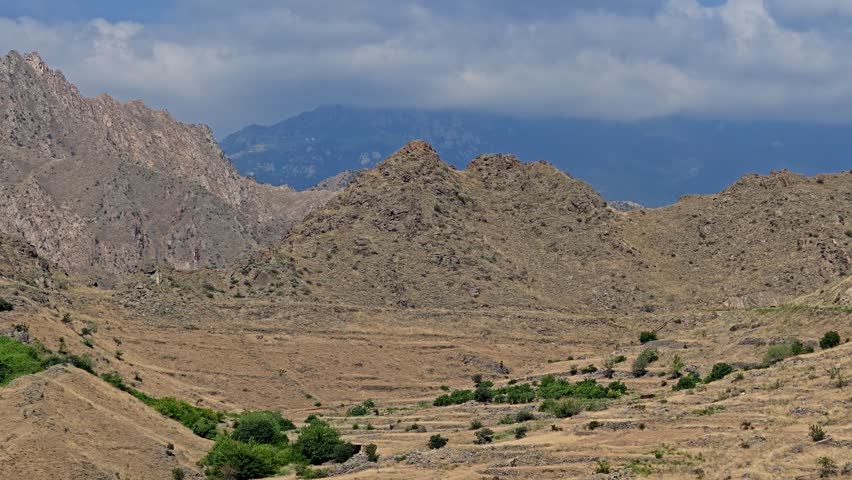 Rugged mountain range under blue sky with scattered clouds. Dry slopes contrast with green shrubs