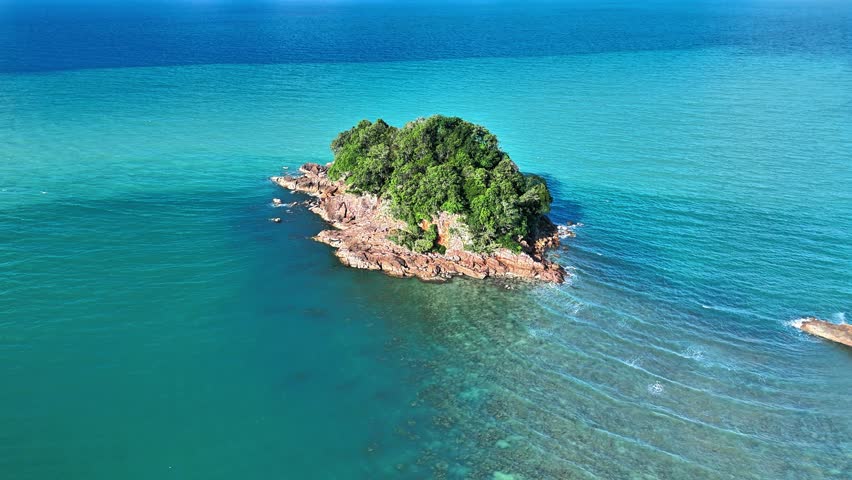 Discover the breathtaking beauty of Punggur Island in Bangka through this high-quality cinematic drone footage, capturing a secluded tropical island surrounded by brilliant turquoise waters and rugged granite formations. The aerial perspective reveals dense green vegetation covering the island while natural rocky shores meet the calm ocean in a striking contrast of color and texture. Gentle waves create delicate patterns across the surrounding sea, highlighting the pristine marine environment and emphasizing the peaceful atmosphere of this untouched destination. The expansive horizon, crystal-clear water, and dramatic coastal scenery combine to create an inspiring visual experience suitable for travel promotions, tourism campaigns, environmental documentaries, nature presentations, commercial advertising, and digital storytelling. Every movement showcases the island