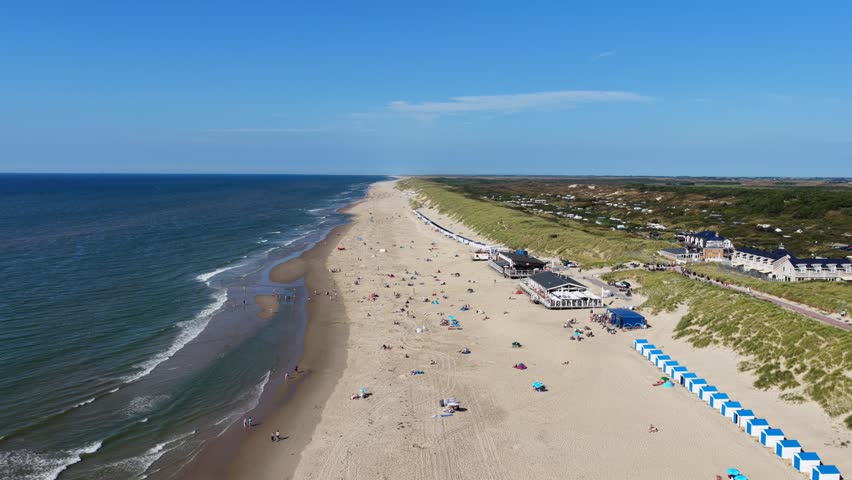 Aerial view of the sandy beach with rows of blue and white beach huts, dunes, and a restaurant along the coastline in De Koog, North Holland, Netherlands.