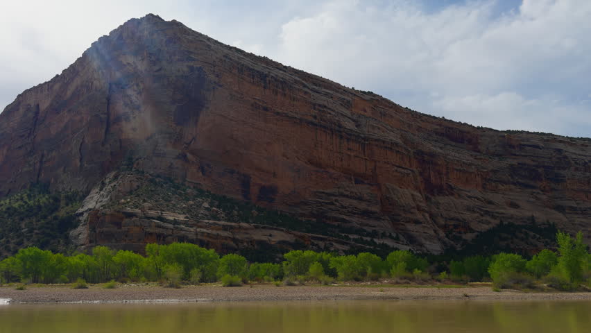 Layered canyon slopes and green riverside vegetation line the Yampa River beneath cloudy skies, Yampa River backcountry experience