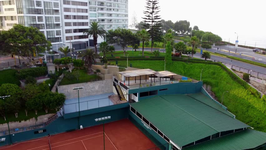Aerial view of a tennis court nestled near a park and modern residential buildings in Miraflores, Lima Province, Peru.