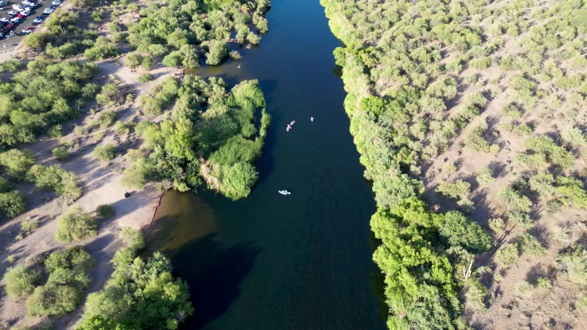 An aerial shot of sunlit kayakers paddling on the dark waters of the Salt River, surrounded by thick desert vegetation in Arizona