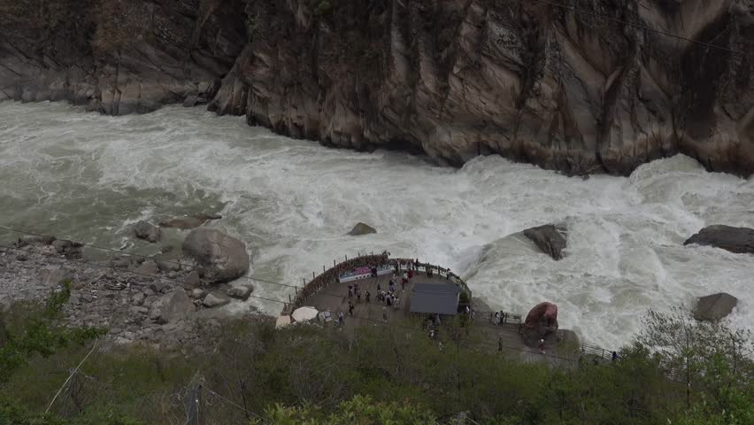 A group of hikers crossing a bridge perched above the turbulent waters of Tiger Leaping Gorge in Yunnan Province, China