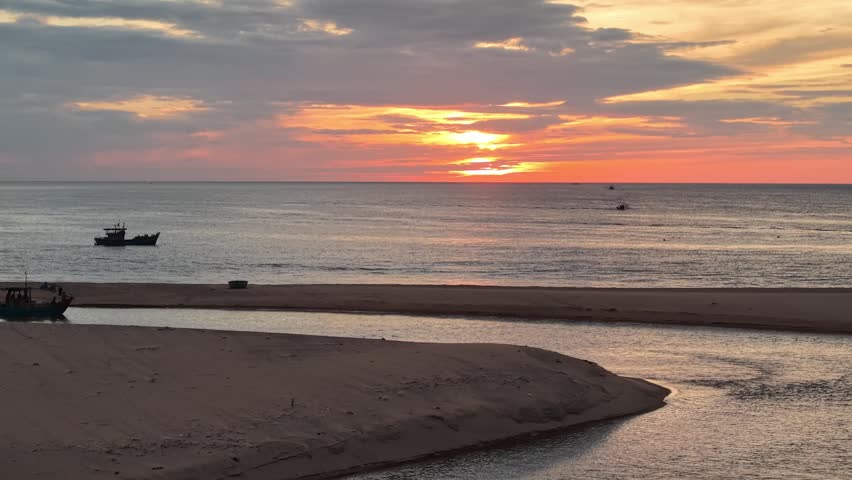 Drone captures the confluence where a river empties into the ocean, with a sandbar separating the waters and fishing boats scattered across the estuary at dawn.