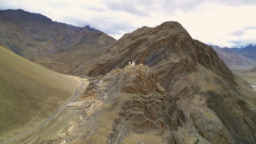 Aerial view of a remote monastery perched on a rugged rocky hill surrounded by the dramatic mountain peaks of the Zanskar valley in Zanskar, Ladakh, India.