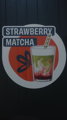 Close-up of a colorful illustrated sign featuring a strawberry matcha drink on a dark wall.